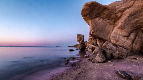 Rock formation on beach against sky during sunset