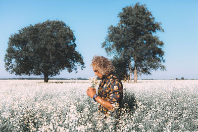 Man smelling flowers while standing against sky