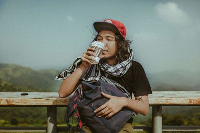 Full length of woman holding cigarette while sitting on railing