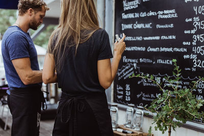 Rear view of businesswoman standing with coworker against wall in restaurant