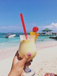 Cropped image of hand holding cocktail drink at beach against sky