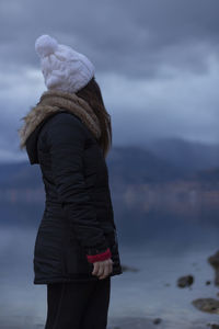 Woman looking away while standing by lake against sky