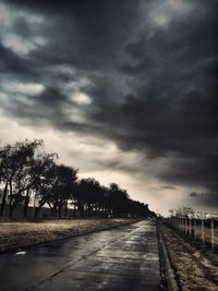 Road amidst trees against storm clouds