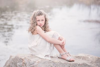 Portrait of a girl sitting on rock by lake