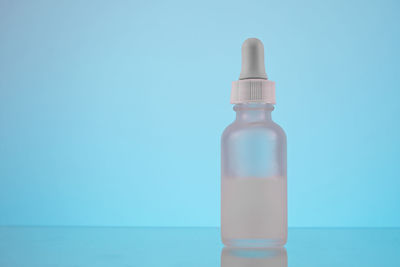 Face serum oil dropper glass bottle with pipette on blue background close up