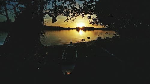 Silhouette trees by lake against sky during sunset