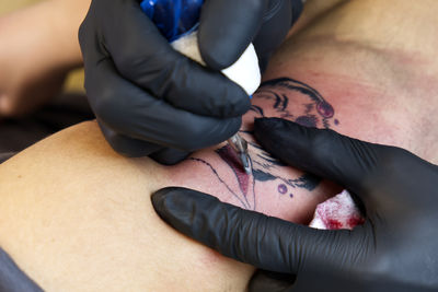 Tattoo artist hands tattooing a caucasian boy's shoulder