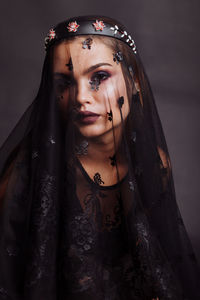Portrait of young woman covered with fabric against black background