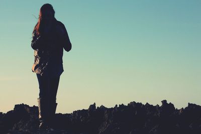 Low angle view of woman standing on rock against sky