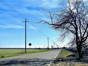 Empty road by electricity pylon against sky