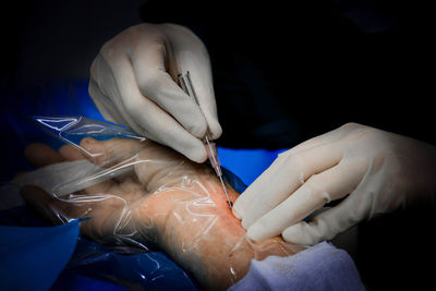 Cropped hands of doctor injecting patient against black background