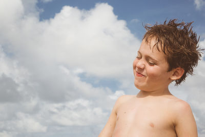 Smiling shirtless boy against sky