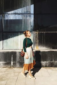 Full length of thoughtful young woman looking away while standing by building