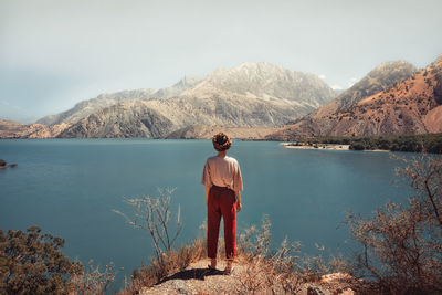 Rear view of man standing by lake against mountain