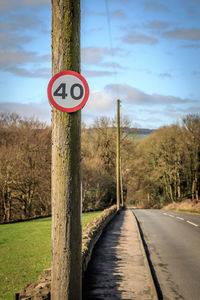 Road sign by trees against sky