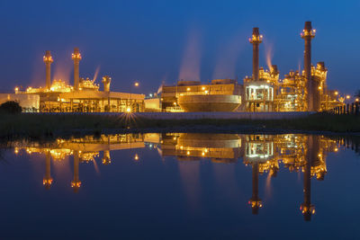 Illuminated factory by river against sky at night