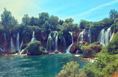 Scenic view of waterfall in forest against sky