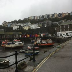 Sailboats moored on harbor by buildings in city against sky