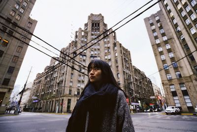 Low angle view of mid adult woman standing on city street against buildings