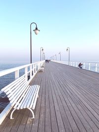 Street lights on pier by sea against clear sky