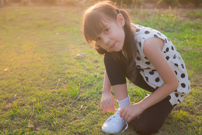 Portrait of girl tying shoelace while crouching on grassy field