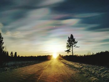 Dirt road amidst field against sky during sunset