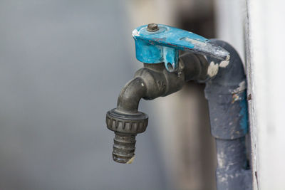 Old blue faucet is on a white wall.