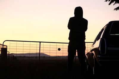 Silhouette man standing by car against sky during sunset