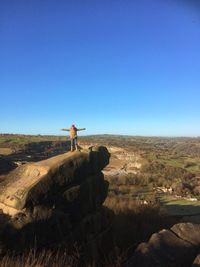 Woman with arms outstretched standing on mountain against blue sky