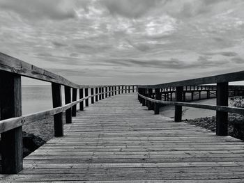 Wooden footbridge on pier over sea against sky