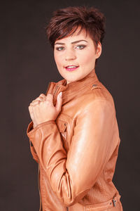 Portrait of female model wearing brown leather jacket against gray background