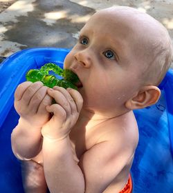 Close-up of shirtless baby boy playing with toy while sitting in bucket