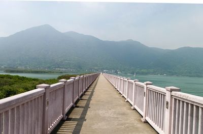 Footbridge leading towards mountains against sky