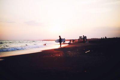 People at beach against sky during sunset