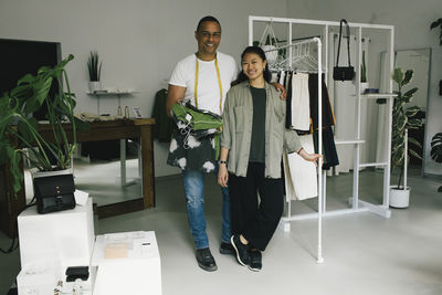 Portrait of smiling male tailor standing with arm around female sales staff near clothes rack at store