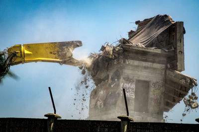 Earth mover demolishing building against clear sky