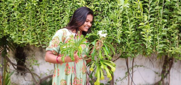 Smiling young woman standing by plants