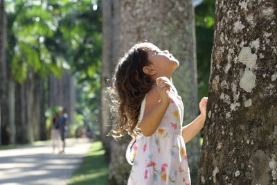 Girl looking up while standing by tree trunk in park