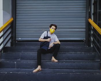 Full length of man wearing mask sitting on staircase