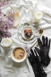 Vogue breakfast in bed with antique tableware, cup of coffee, chocolate profiterole, lilac flowers.