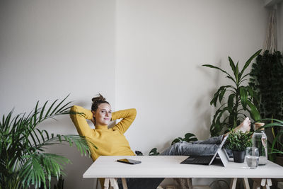 Smiling woman with hands behind head resting while sitting at home office