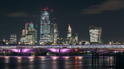 Illuminated buildings by river against sky at night