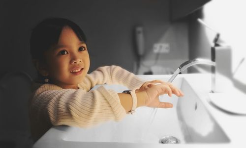 Cute girl washing hands in sink at home