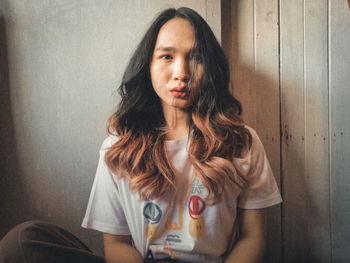 Portrait of young woman sitting against wall