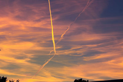 Low angle view of vapor trails in sky during sunset