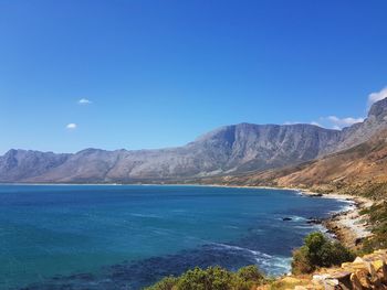 Scenic view of sea and mountains against clear blue sky