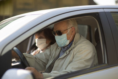 Senior couple wearing anti virus masks are driving in a car during the covid-19 pandemic