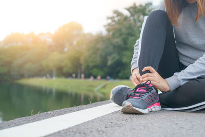 Midsection of woman sitting by lake against trees