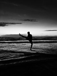 Silhouette young man jumping at beach against sky during sunset