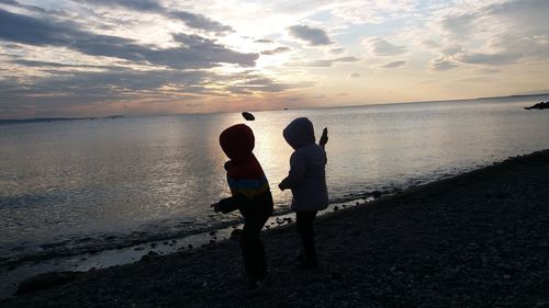 Friends standing on beach against sky during sunset